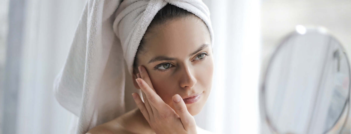Woman with a towel wrapped around her head looking at herself in the mirror.